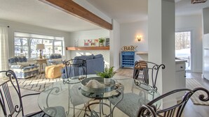 A modern living room with a glass dining table, blue and white patterned sofas, and a wooden ceiling beam.