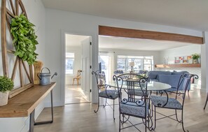 A spacious living area with a dining table and chairs, a sofa, and a wooden ceiling beam.