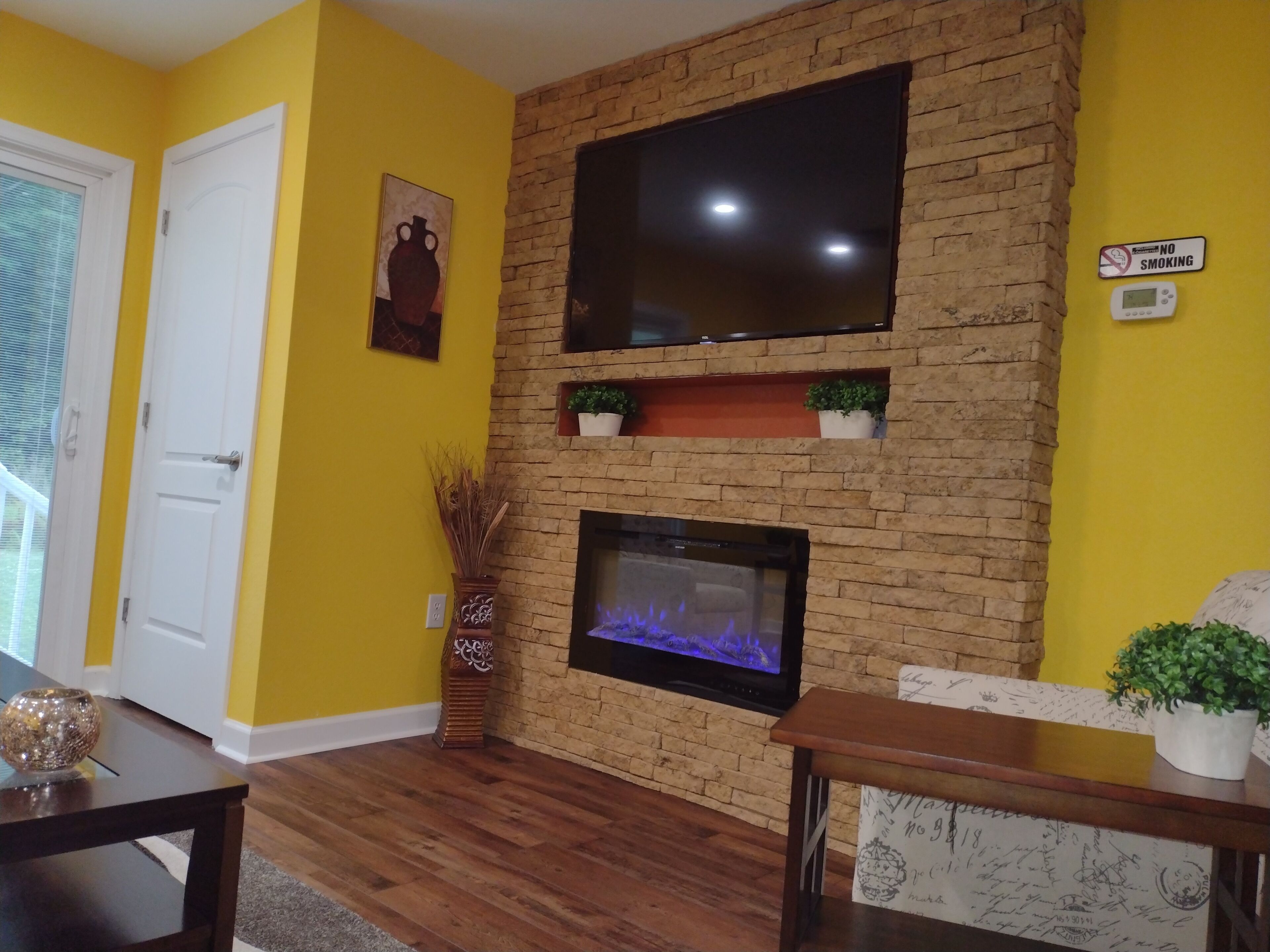 Un salon avec une cheminée en briques, un téléviseur à écran plat fixé au-dessus, et un panneau « Il est interdit de fumer » accroché au mur.