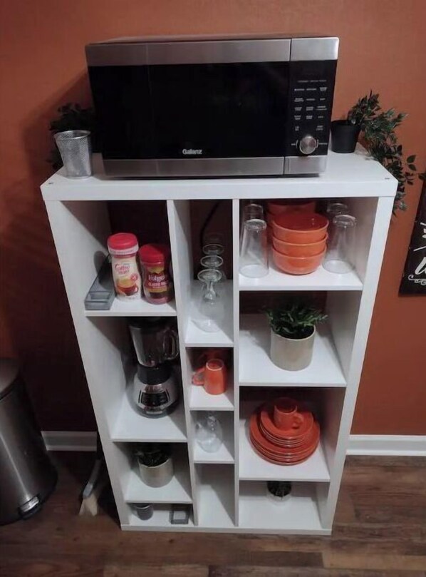 A white storage unit with a microwave on top, containing kitchenware and containers.