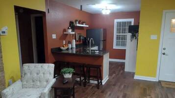 Un espace de vie compact comprenant un coin repas, une kitchenette et une porte donnant sur une autre pièce.