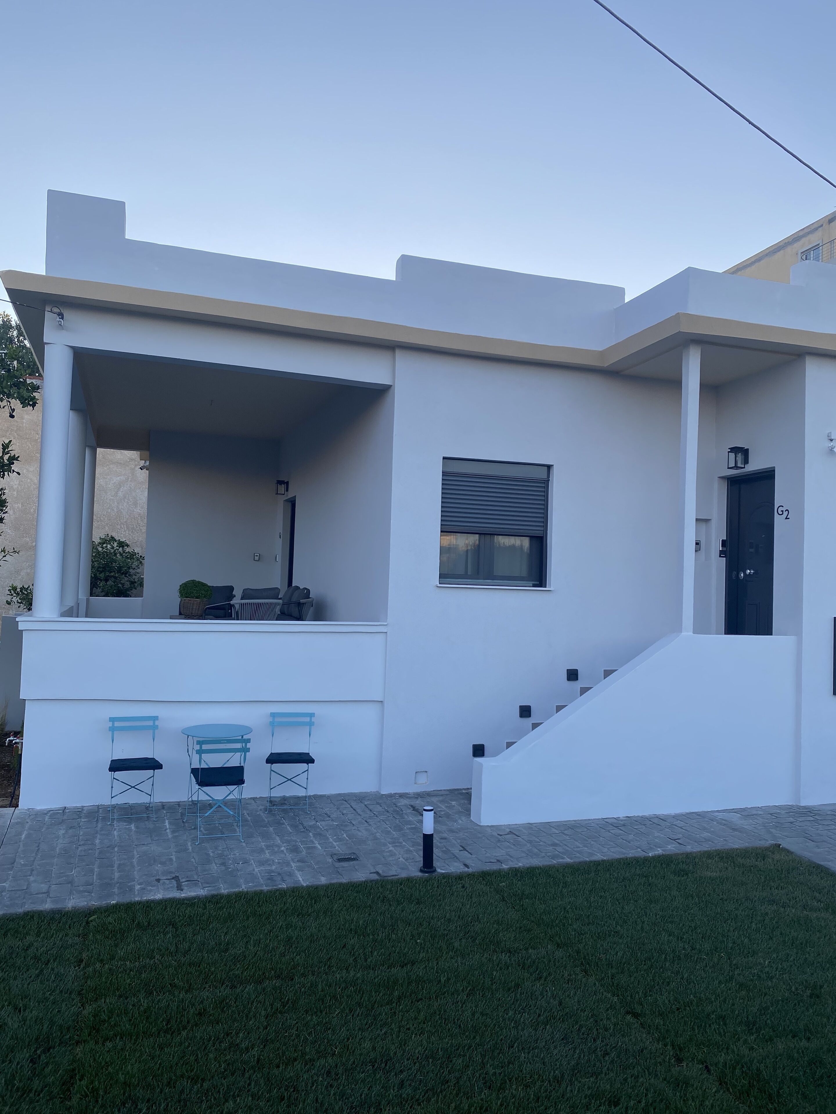 A modern house with a flat roof, a covered porch with seating, and a staircase leading to the entrance.