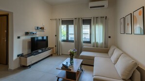 A modern living room with a flat-screen TV, a sofa, a coffee table with books, and a vase with flowers. - Galio Suites Airport by Airstay (Spata-Artemida)
