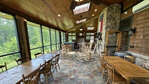 Un espacio interior amplio con ventanas grandes, mesas y sillas de madera, suelo de piedra y una chimenea de piedra.