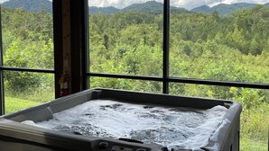 Un jacuzzi con vista a una cadena montañosa boscosa a través de amplios ventanales.