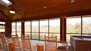 Interior de madera con mecedoras, bañera de hidromasaje y ventanas amplias que ofrecen vistas al exterior.