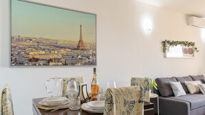 Un coin repas avec une table dressée pour quatre personnes, un tableau représentant la Tour Eiffel et un canapé gris en arrière-plan.