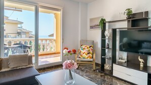 Un salon avec un balcon, un canapé, un fauteuil, une télévision et une bibliothèque.