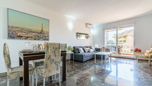 Un salon moderne comprenant un coin repas, un canapé, une table basse et une grande fenêtre donnant sur des immeubles.