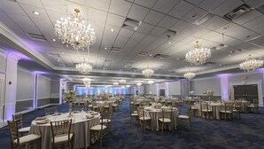Un salón de banquetes con mesas redondas, sillas, candelabros y suelo alfombrado.