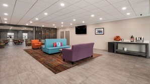 Un vestíbulo amplio con una recepción, un sofá azul, un sillón naranja y un sofá púrpura.