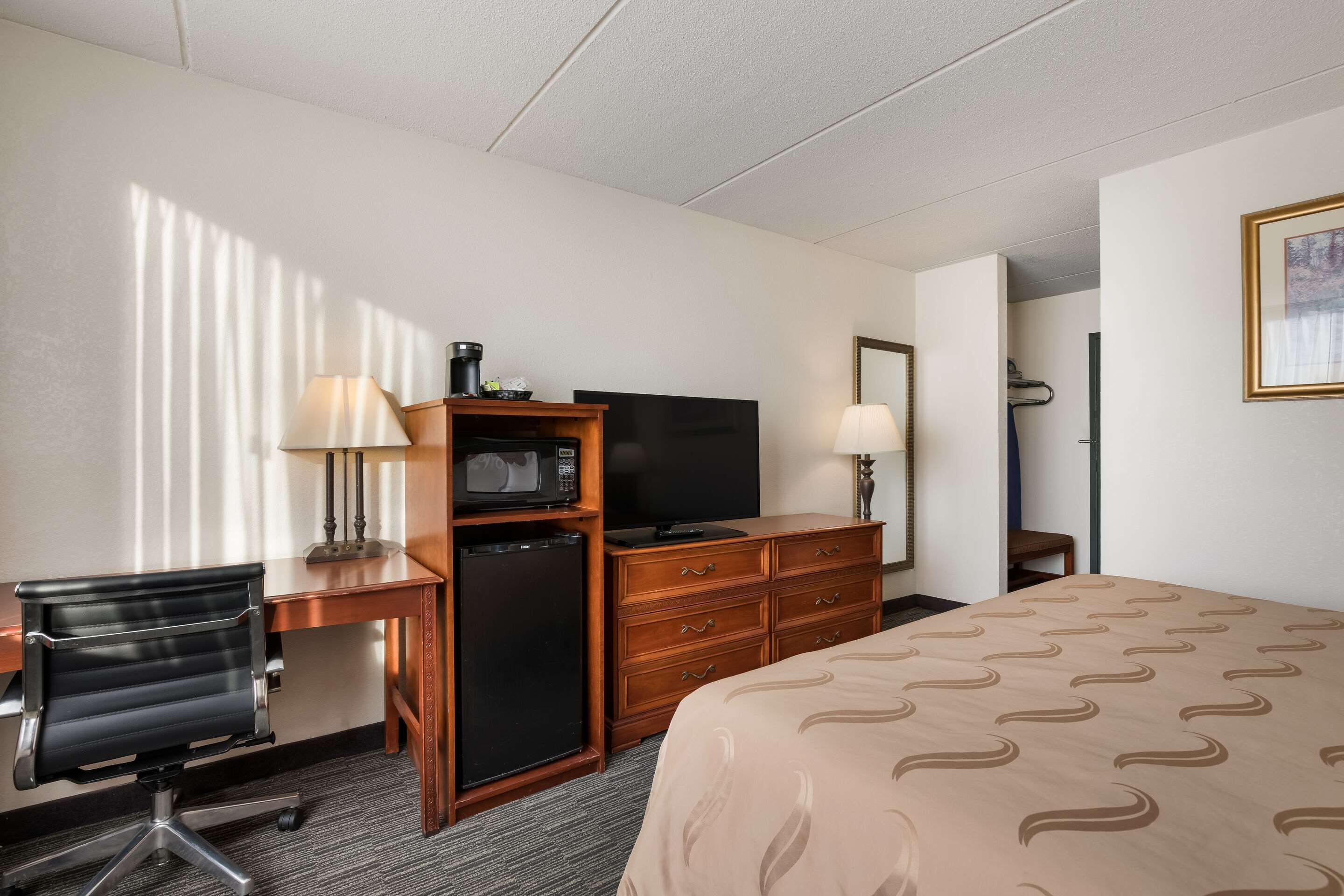 Une chambre d’hôtel équipée d’un lit, d’un bureau, d’une chaise, d’une télévision, d’un four à micro-ondes et d’une commode.