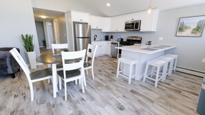 A modern kitchen with white cabinetry, stainless steel appliances, and a central island with bar stools. - Enjoy the beach during the day and sunsets at night (Seabrook)