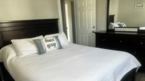 A neatly made bed with a white quilt and two pillows, one with a beach house design. - Enjoy the beach during the day and sunsets at night (Seabrook)