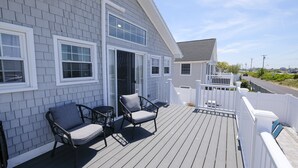 A deck with two chairs and a glass door leading to a house with white trim and grey siding. - Enjoy the beach during the day and sunsets at night (Seabrook)