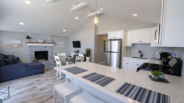 A modern kitchen with white cabinets, a stainless steel refrigerator, and a dining area with a white table and chairs. - Enjoy the beach during the day and sunsets at night (Seabrook)