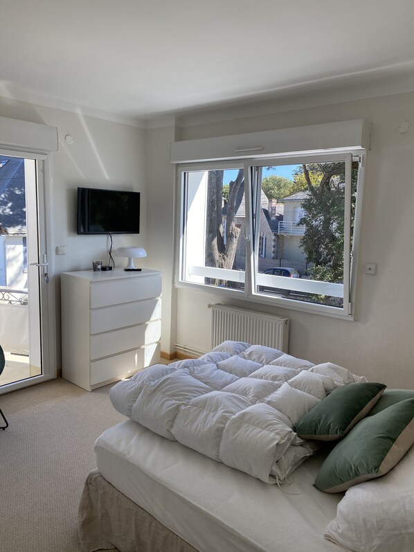 A bedroom with a bed, a dresser, a TV, and a window with a view of the outside.