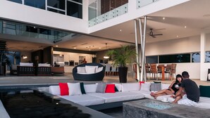 Un espace de vie extérieur moderne, doté d’une piscine, de coins salon et d’une cuisine en arrière-plan.
