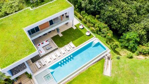 Une maison moderne dotée d’un jardin sur le toit, d’une piscine et d’un patio aménagé avec du mobilier d’extérieur.
