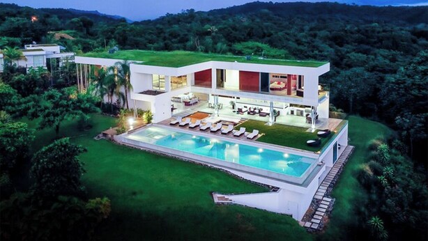 Une maison moderne dotée d’une piscine, entourée d’une végétation luxuriante et de collines.