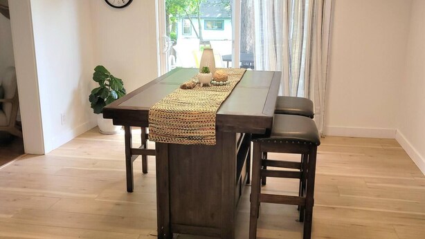 Una zona pranzo con tavolo in legno, due sedie, un orologio a parete e una finestra con tende.