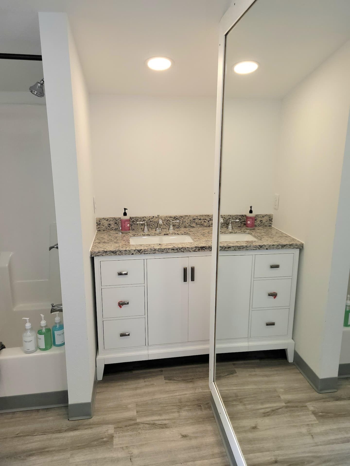 Une salle de bain moderne avec un comptoir en granit, des meubles blancs et un grand miroir.