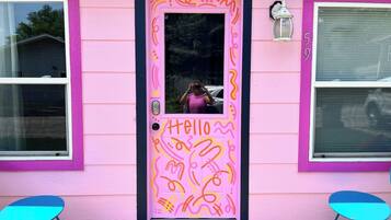 Una casa rosa con una porta decorata da insegne con la scritta 'Hello' e motivi astratti.