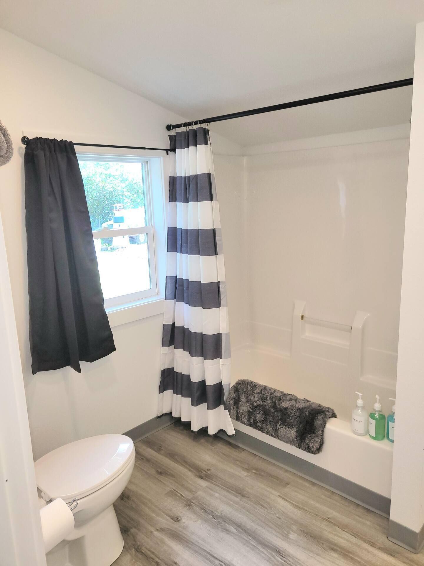 Une salle de bain comprenant des toilettes, une douche avec un rideau rayé noir et blanc, une baignoire et une fenêtre donnant sur les arbres.