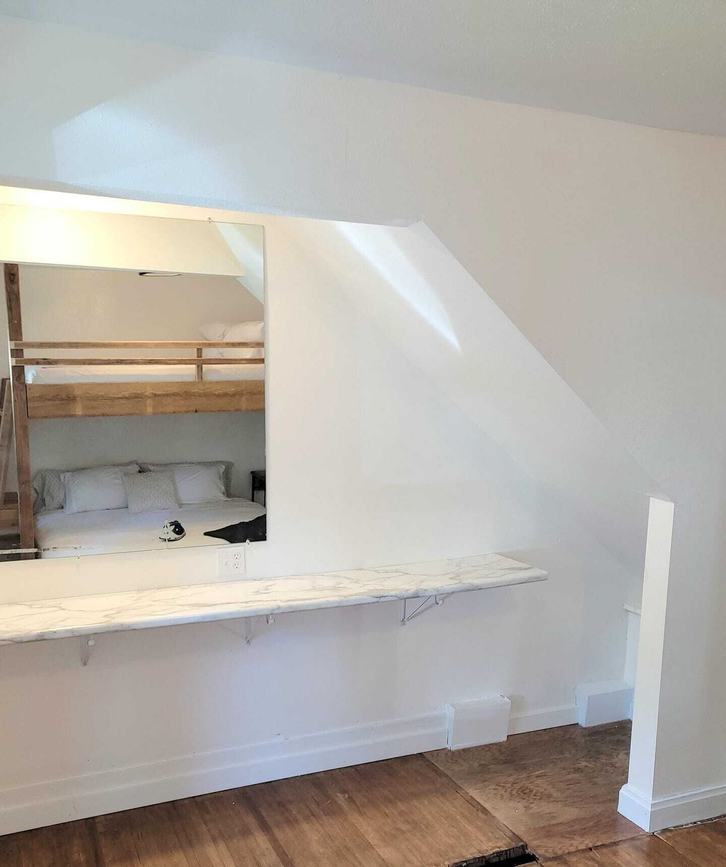 Een slaapkamer met een stapelbed, een klein nachtkastje en een spiegel.