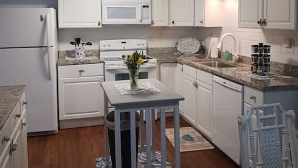 A compact kitchen with white cabinets, a microwave, a stove, and a sink. There's a small table with a vase and a rug. - Park Ave Peacock in the heart of Cleveland TN (Cleveland)