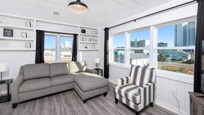 Een moderne woonkamer met een grijze modulaire bank, een gestreept fauteuil en een groot raam met uitzicht op gebouwen.