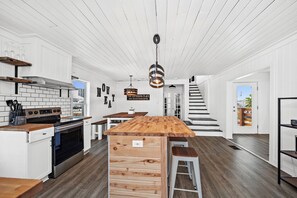 Une cuisine moderne avec des meubles blancs, un îlot central et un escalier menant à un balcon.