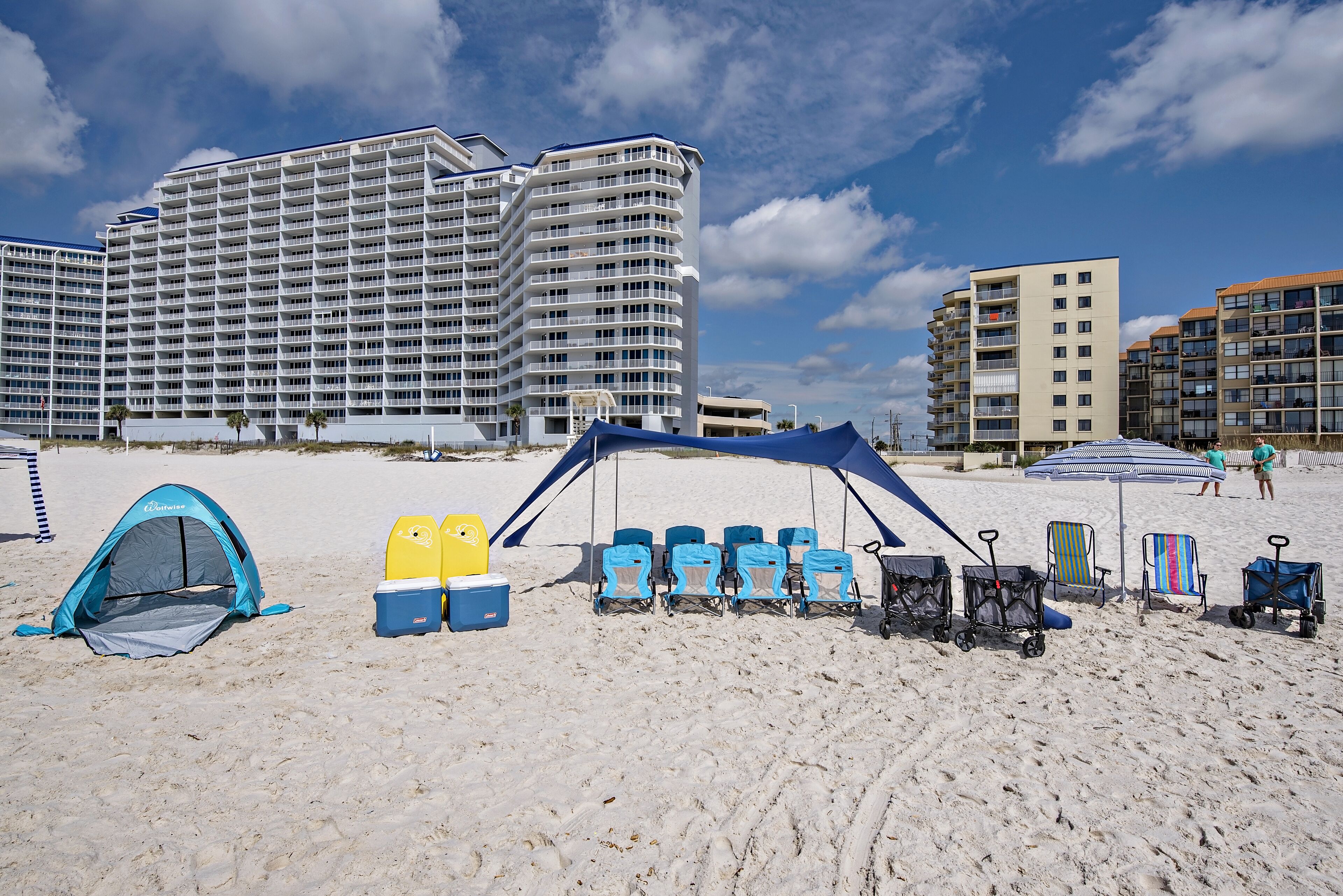 A beach with a tent, beach chairs, and umbrellas. There are high-rise buildings in the background.