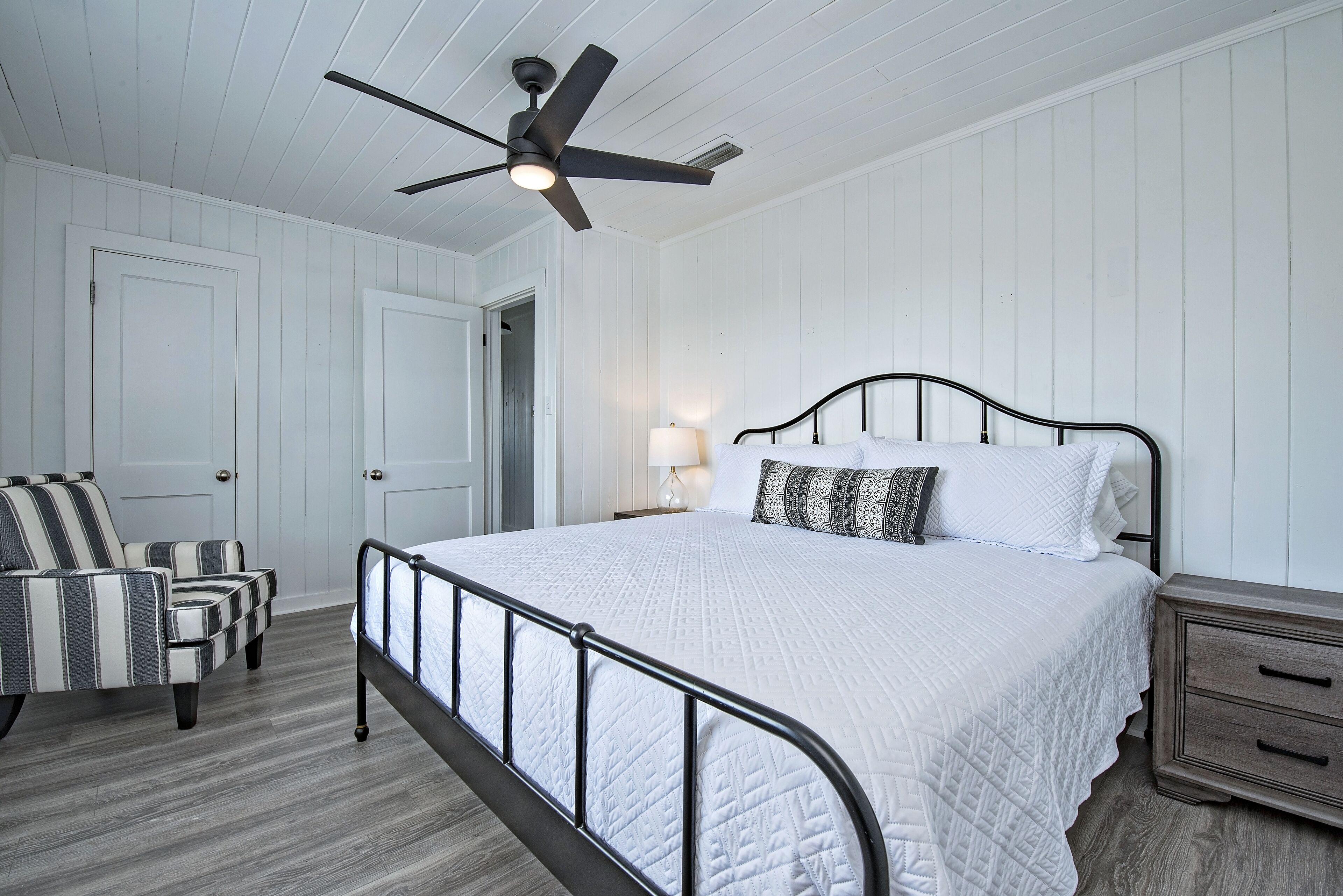 A bedroom with a bed, a chair, a nightstand, and a ceiling fan.