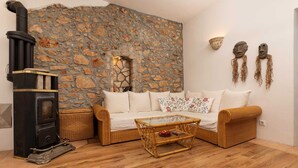 A cozy living room with a stone wall, a black wood stove, a wicker sofa, and a coffee table. - Villa O'Lucky with pool and unique tavern "konoba" (Polje (Krk))