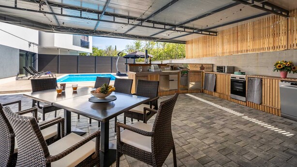 Un espace cuisine extérieur avec une piscine, une table à manger et des chaises.