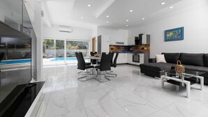 Un salon moderne avec une table basse en verre, un canapé et un coin repas offrant une vue sur la piscine.
