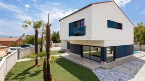 Une maison moderne à deux étages, dotée d’un toit plat, de grandes fenêtres et d’une piscine située dans le jardin arrière.