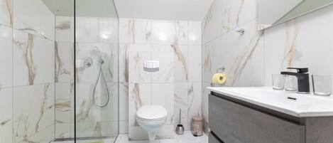 Une salle de bain moderne dotée d’une douche à parois de verre, de toilettes et d’un meuble-lavabo avec un évier.