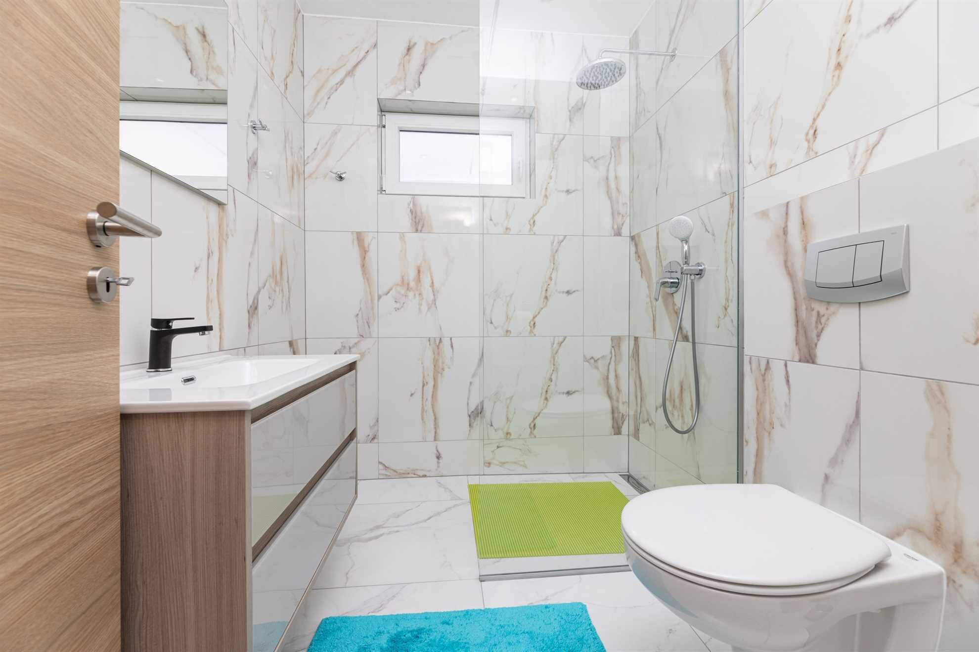 Ein modernes Badezimmer mit Marmor-Spritzschutz, einer Dusche, einer Toilette und einem Waschbecken mit Holzkabinent.
