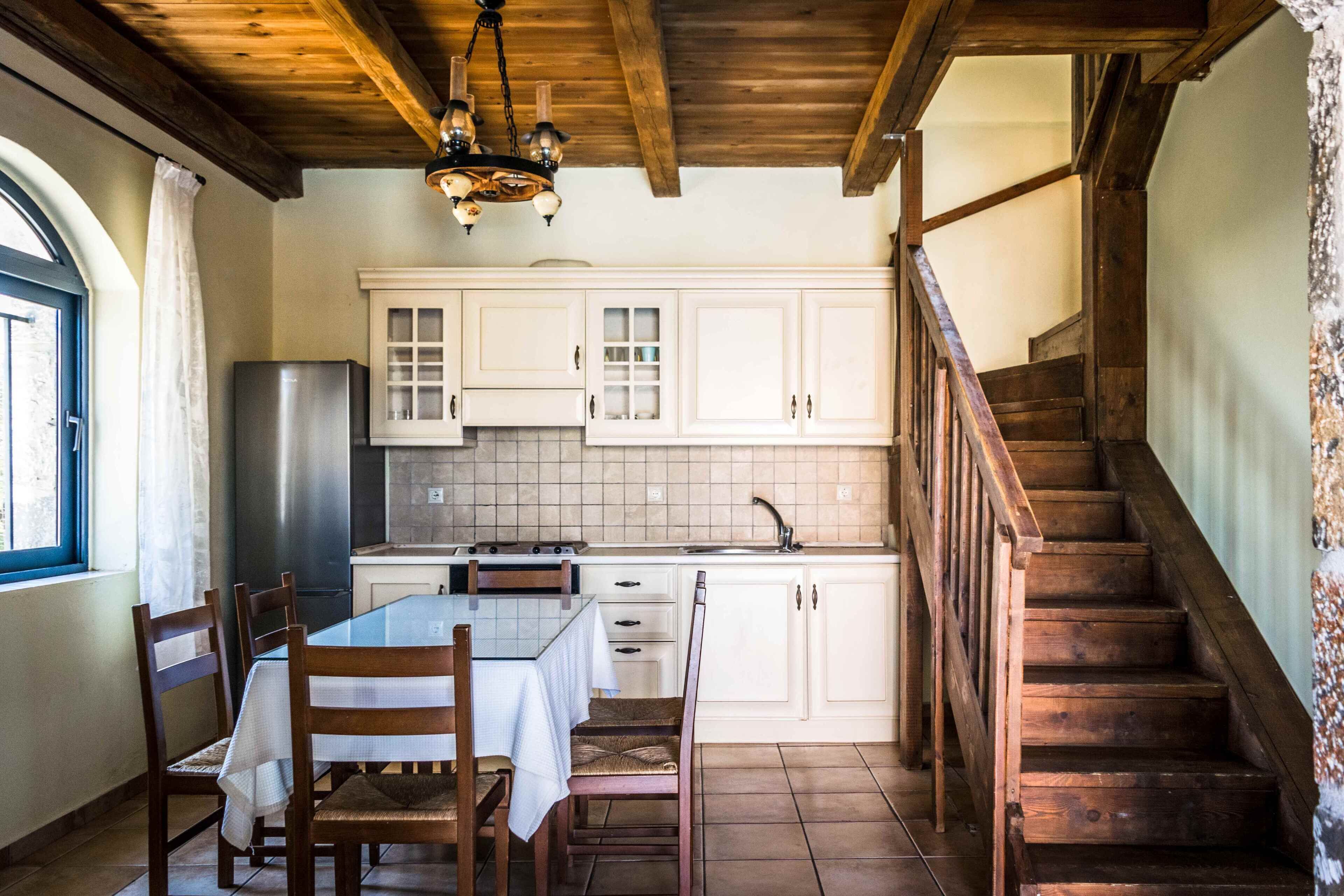 Eine Küche mit weißen Schränken, einem Holzespeisetisch, Stühlen, einer Kandelaber und einer Holztreppe.