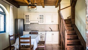 Une cuisine avec des meubles blancs, une table à manger en bois, des chaises, un lustre et un escalier en bois.