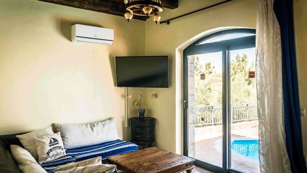 Un salon comprenant un canapé, un téléviseur à écran plat, une table basse en bois et une porte-fenêtre coulissante donnant sur un espace extérieur avec une piscine.