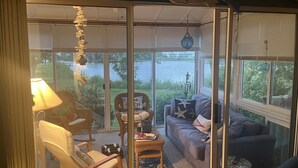Una sala de estar acogedora con vista a un lago, amoblada con un sofá, sillas y una lámpara.