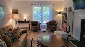 A living room with a sofa, two armchairs, a coffee table, a fireplace, a TV, and a bookshelf. - Highland Comfort - Private Peaceful Retreat (Chapel Hill)