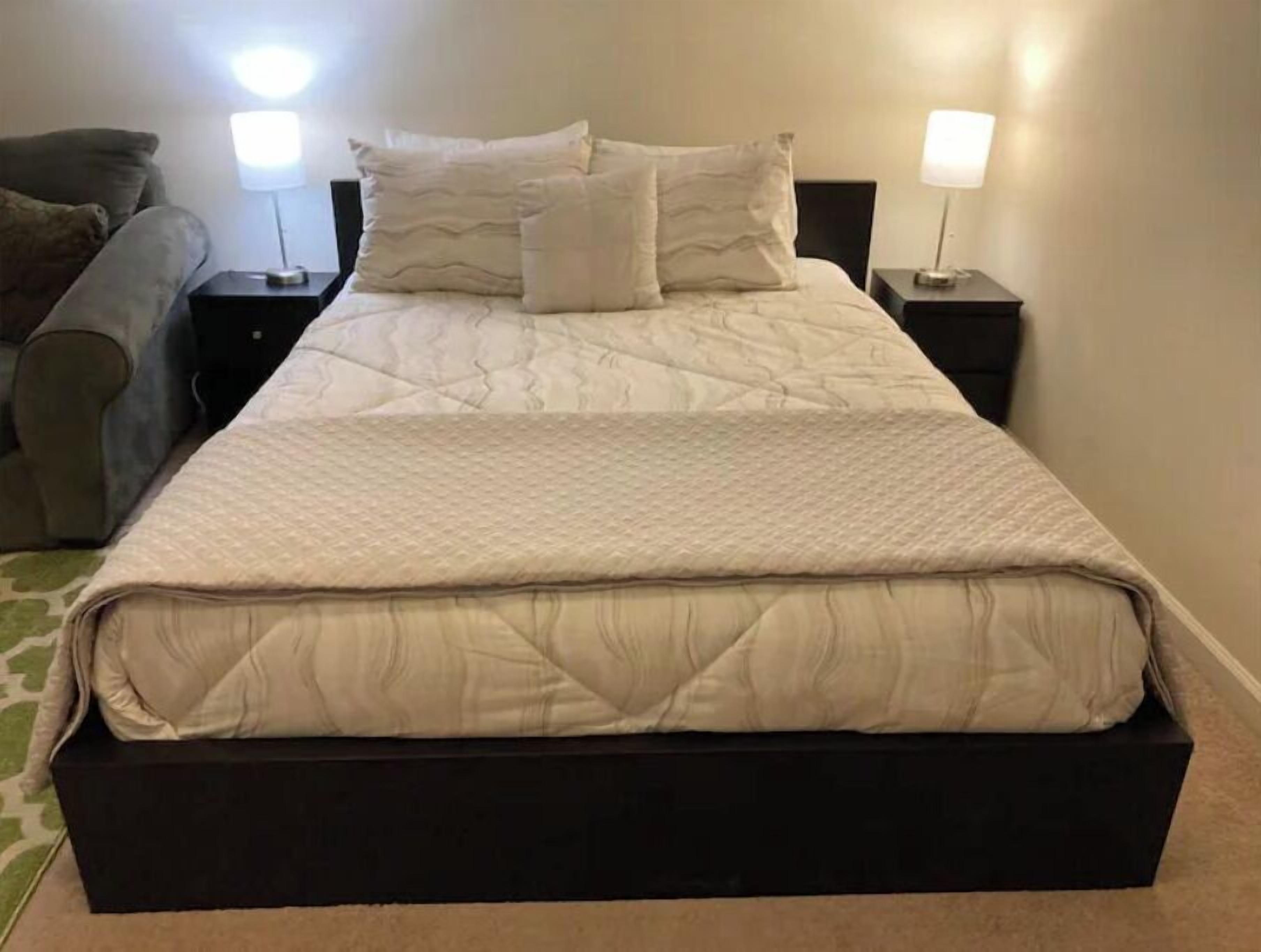 Un letto rifatto con copriletto trapuntato, due comodini con lampade e un divano sullo sfondo.