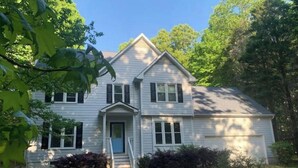 A two-story house with a front porch, a central entrance, and a small front yard with bushes. - Highland Comfort - Private Peaceful Retreat (Chapel Hill)