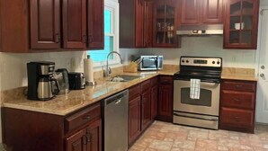 A kitchen with wooden cabinets, a dishwasher, a stove, a microwave, and a coffee maker. - Highland Comfort - Private Peaceful Retreat (Chapel Hill)