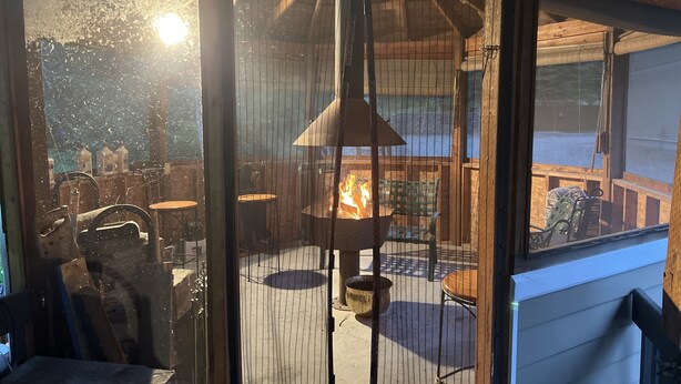 Un espacio al aire libre acogedor con un brasero, rodeado de mobiliario de madera y una cerca de metal.
