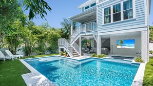 A two-story house with a swimming pool, a covered patio, and a large TV screen. - Paradise Blu by Beach Boutique Rentals (Anna Maria)